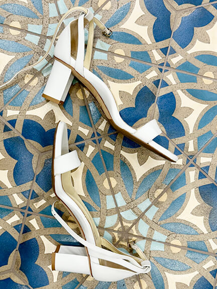 New England interior designer styling white block sandals with arch support on blue and green Mediterranean tile.
