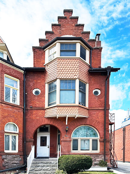 Queen Anne Revival home in Toronto with stepped roofline, arched brick details, round and bay windows, and a bold, geometric silhouette