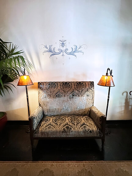 Damask settee with stenciled walls and antique lamps in the entryway of Chateau Marmont, blending vintage style with historic architecture.