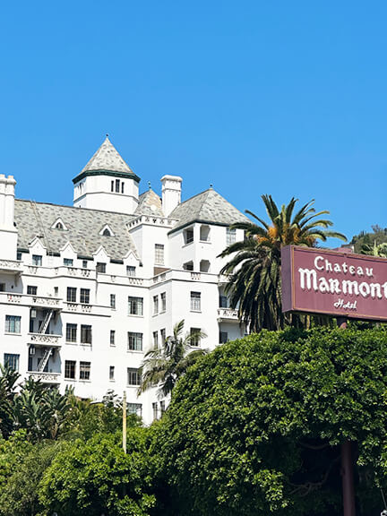 Chateau Marmont’s white building with vintage faded signage surrounded by lush greenery, showcasing historic Hollywood charm.