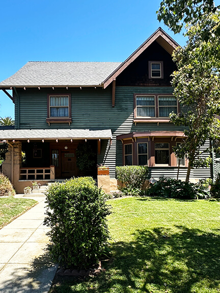 Historic home in Koreatown, Los Angeles, with green-painted exterior architecture, lush plantings, and early 20th-century details.
