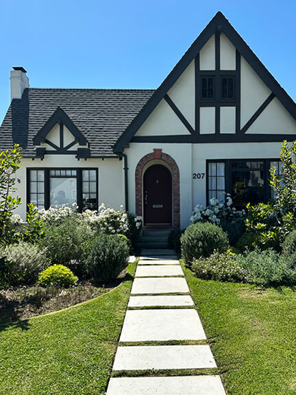 Tudor Revival cottage in Los Angeles with half-timber detailing and steep rooflines, nestled among lush greenery and mature plantings.