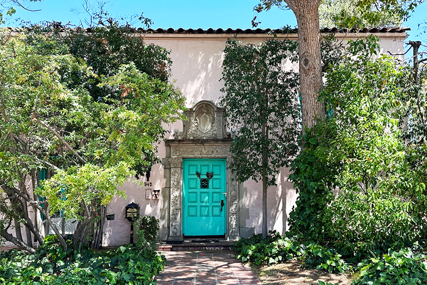 A charming pink stucco house with a bright teal door and minimal trim details, located in Windsor Square near Hancock Park, LA.