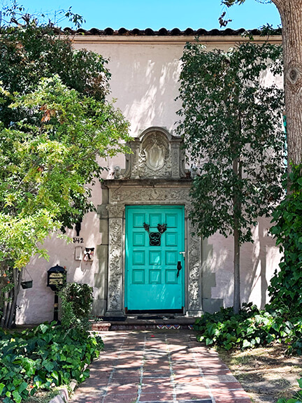 Historic architecture in Los Angeles captured in a pink stucco home with teal door, natural stone detailing, and a lush garden.