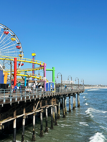 Ferris wheel and rollercoaster on the Santa Monica Pier, with colorful signage and views of the Los Angeles coastline.