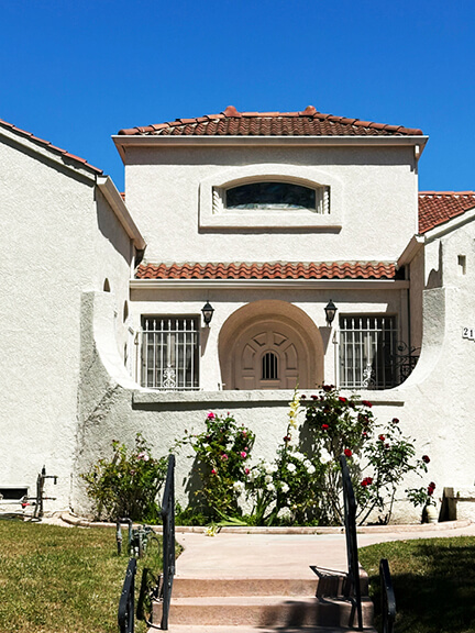 Historic architecture in Los Angeles shown in a stucco home with a terracotta tile roof and arched openings in a revival style.